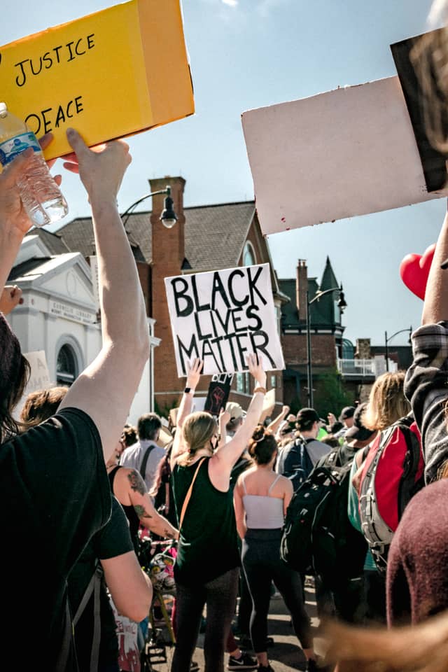 A woman holds a protest sign that says Black Lives Matter in a crowd of others protesting with her