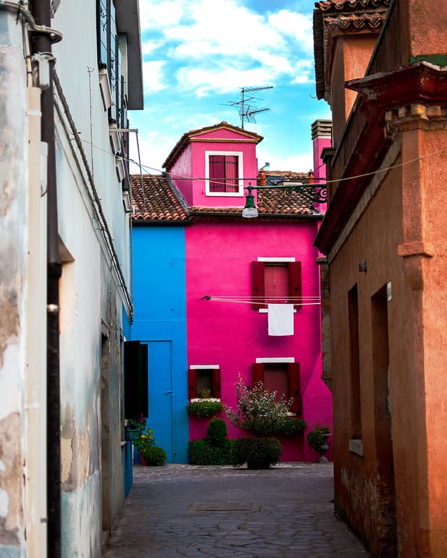 A building painted half blue and half pink is framed by another building to the left and right