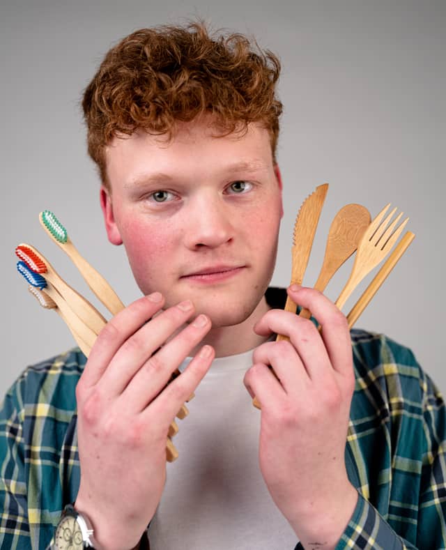 Head on portrait of a man holding up 4 toothbrushes and a set of bamboo utensils