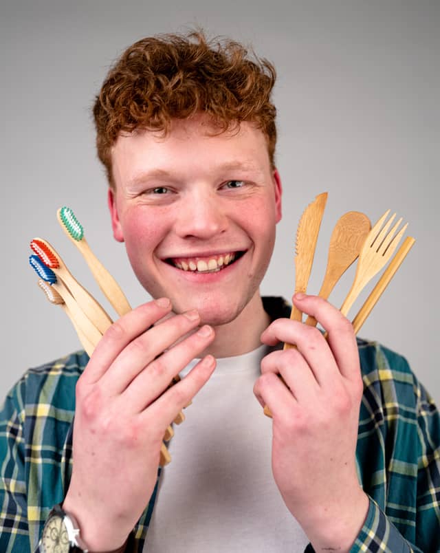 Head on portrait of a man holding up 4 toothbrushes and a set of bamboo utensils