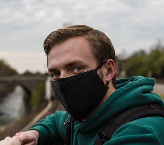 Head on portrait of a man leaning over a railing with a black facemask on