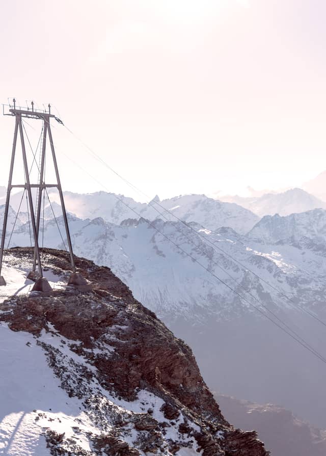 Electrical infrastructure lines are shown scaling down a mountain with snow covered alps in the background