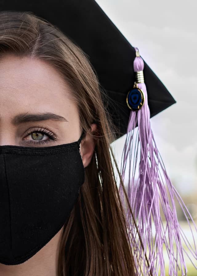 Head on portrait of a woman with a black facemask on and a graduation cap