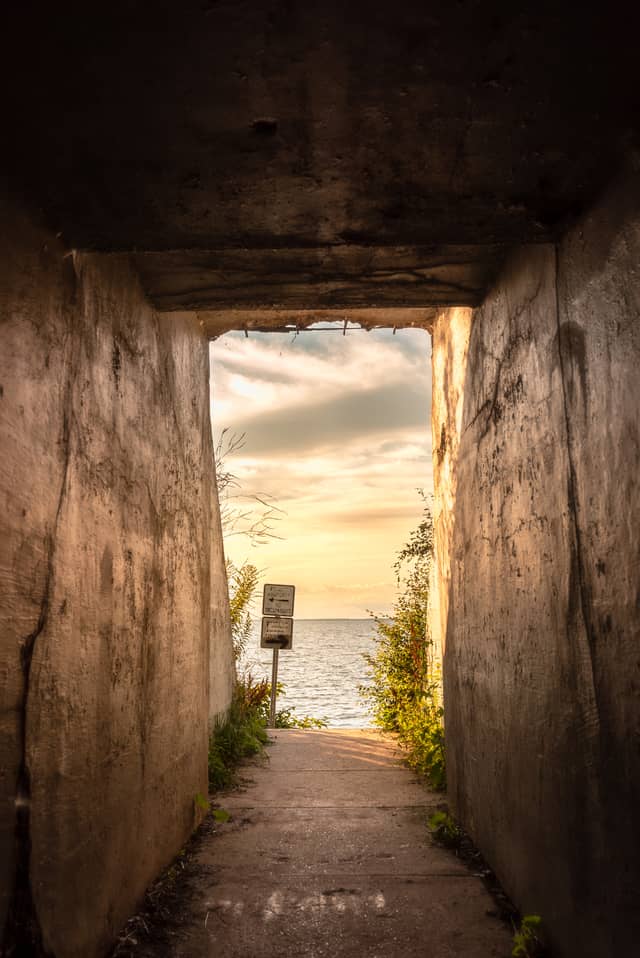 A lake is shown at the end of a concrete tunnel that has a 'No Trespassing' sign at the end