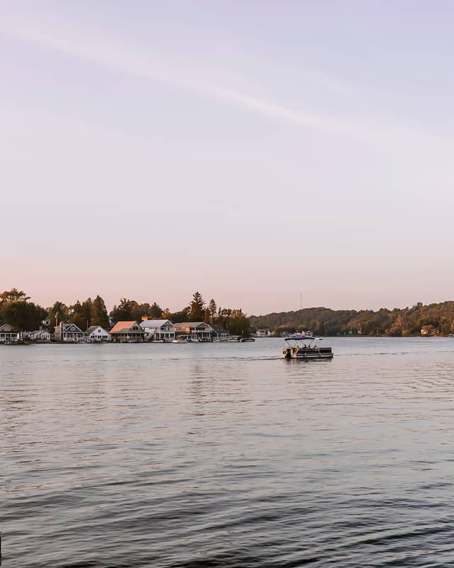 A pontoon boat is shown traversing a lake at sunset