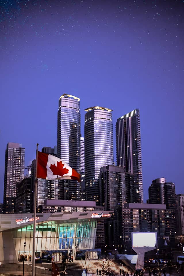 Three skyscrapers under a sky of stars, with a canadian flag in the foreground