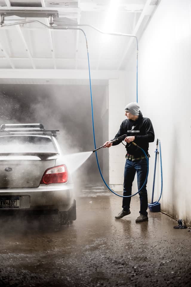 A man is washing the side of his car with a car wash sprayer