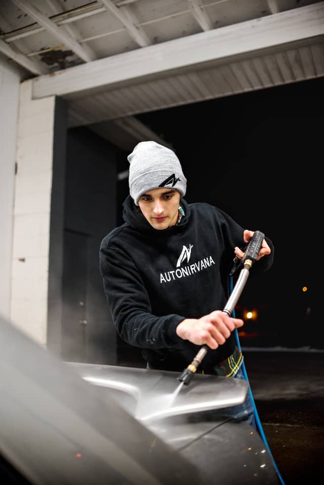 A man is washing the back of his car with a car wash sprayer