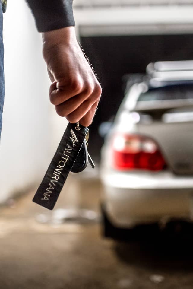 A man is holding a jet tag that says 'AutoNirvana' in front of his car
