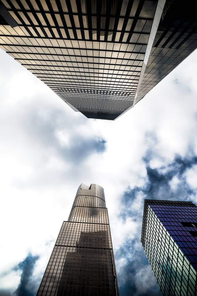 Three skyscrapers are shown looking straight up with a blue cloudy sky in the background