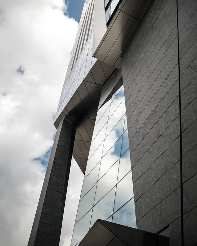 A skyscraper with pointed, geometric windows is shown against a blue cloudy sky