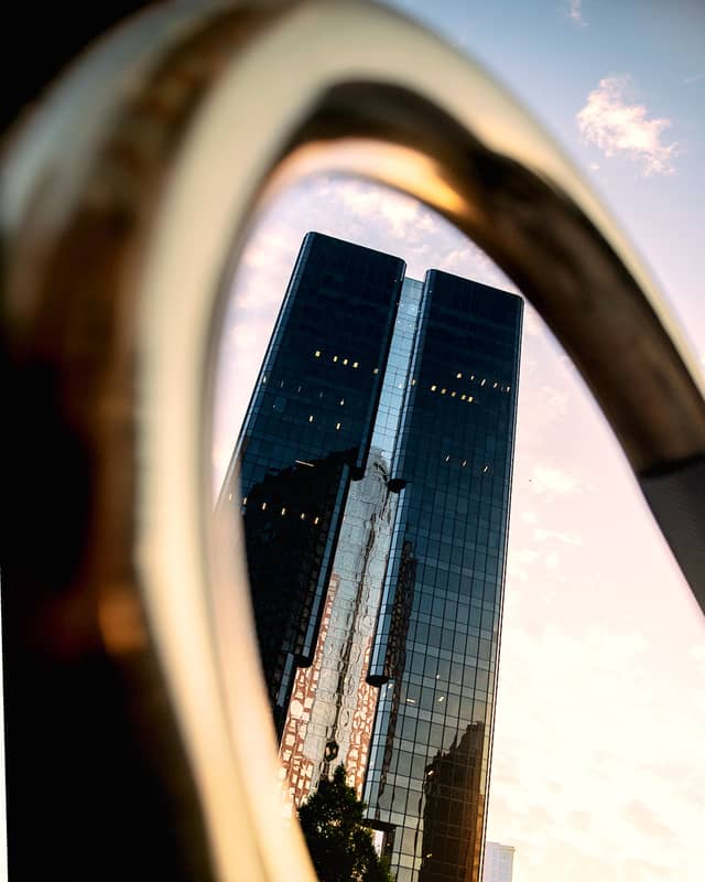 A skyscraper is viewed through a curved gold railing