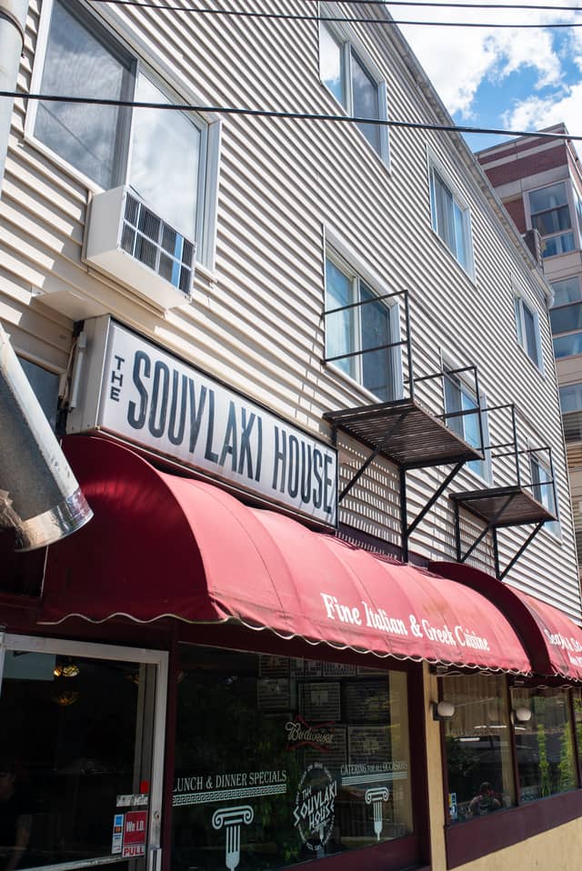 A tan apartment building is shown with a restaurant underneath with a sign that says 'The Souvlaki House'