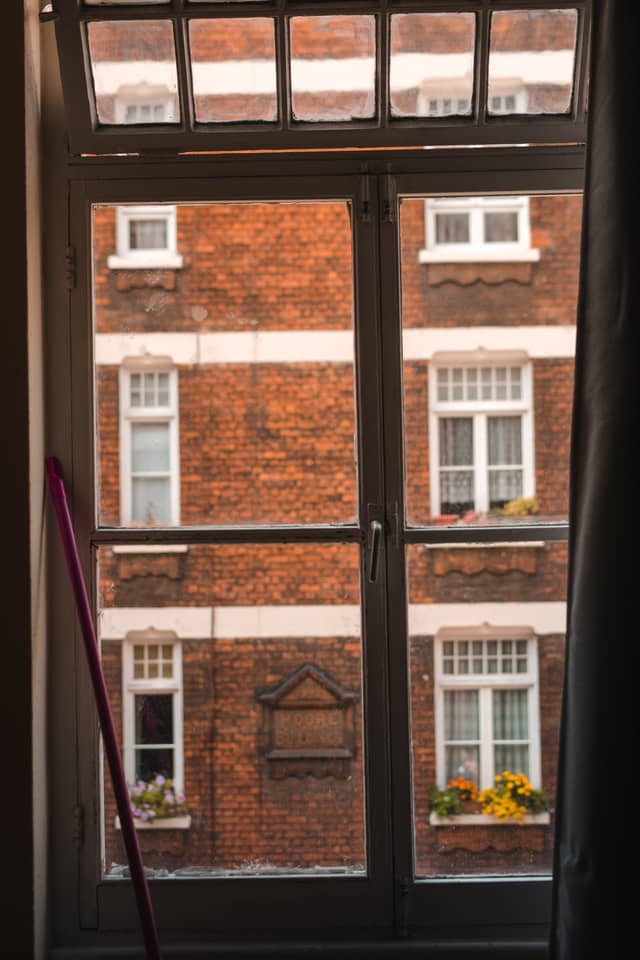 An old brick apartment building is viewed through a large-paned window