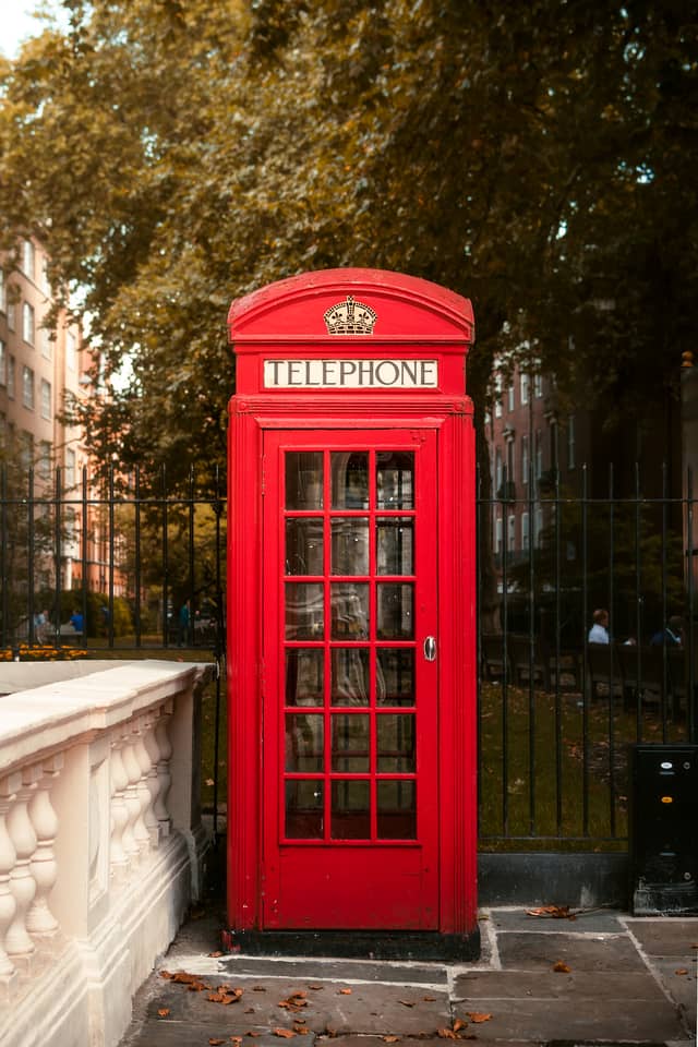 A bright red telephone booth is shown centered with a park behind it