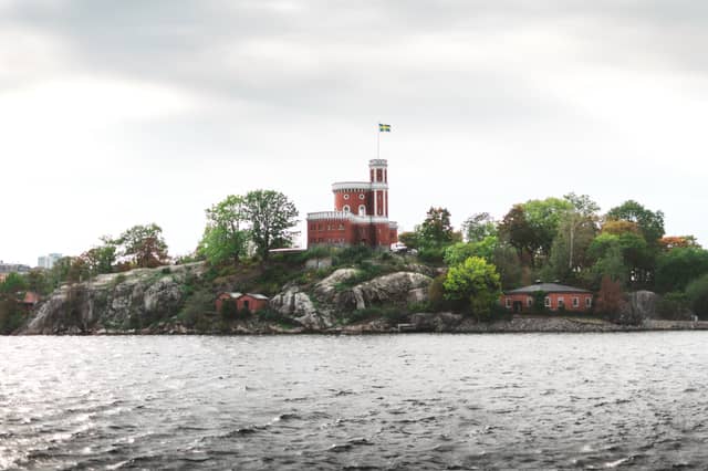 A red castle with a Swedish flag is centered on a large stone outcropping on a body of water