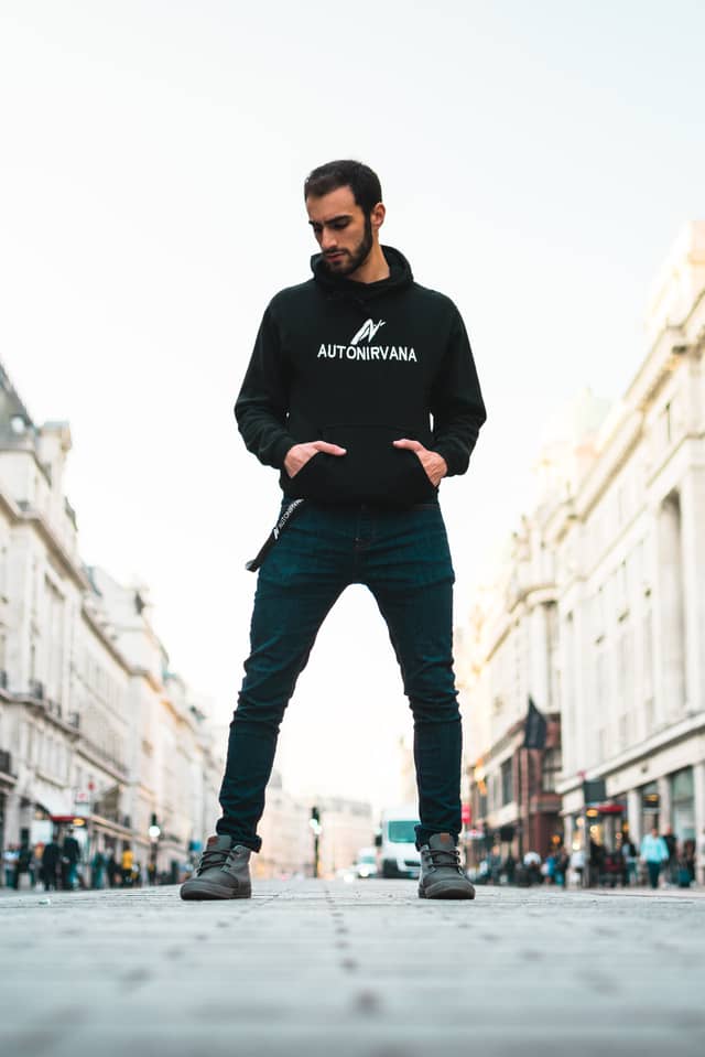 A man is standing on a sidewalk, looking down, posing for a photograph