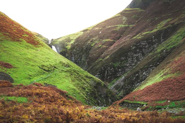 A small waterfall flows over grass-lined hills