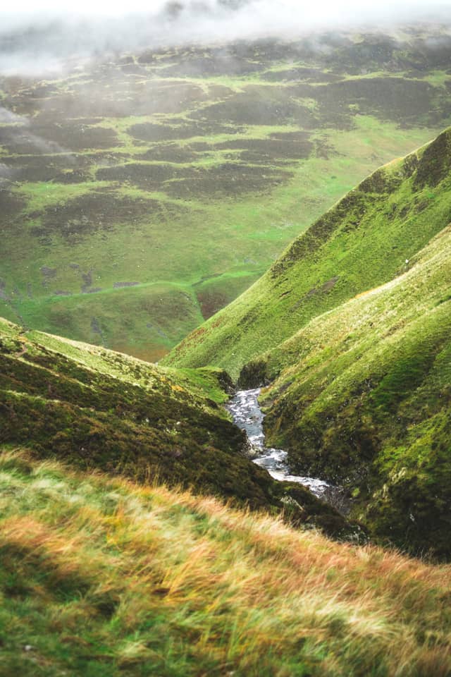 A small waterfall flows over grass-lined hills