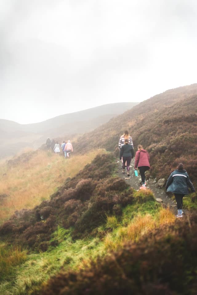 A group of people walk down a dirt path over rolling hills