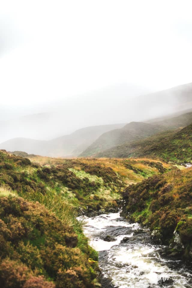 A small waterfall flows over grass-lined hills