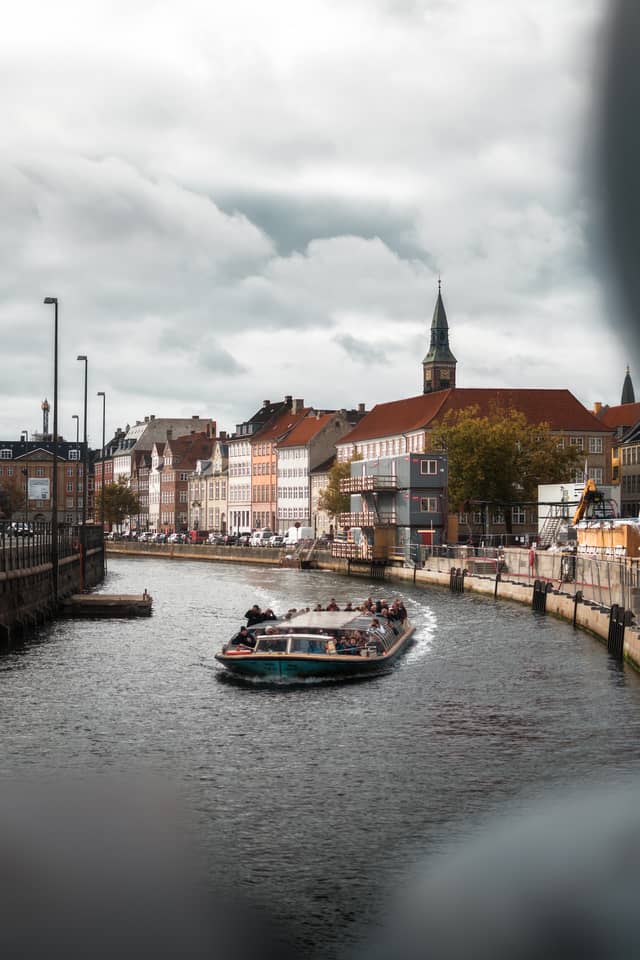 A sight-seeing boat glides along a canal flanked by side-by-side old apartment buildings