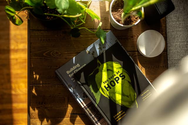 A book called 'The Book of Hops' is photographed sitting on an endtable surrounded by houseplants